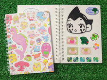 Load image into Gallery viewer, one spiral-bound notebooks with a colorful cartoon character pattern, placed on a green grass-like surface. behind it, there is an open notebook showing the sticker-collecting wax paper inside.
