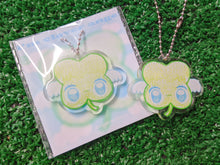 Load image into Gallery viewer, a cute, cartoonish four-leaf clover charm keychain with white wings and blue eyes, attached to a silver ball chain

to the left is the same keychain on the cute backing card it comes on
